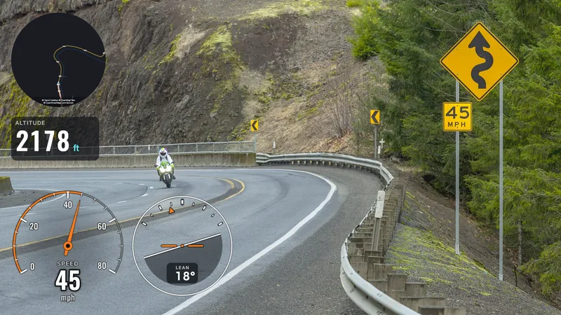 A photo of a bend on a mountain road with a motorcyclist, a winding-road sign and a 45 mph sign on the right; a round dark map with the track top left, altitude (2178 ft) below it, a needle speedometer at 45 mph and a lean indicator at 18° at the bottom.